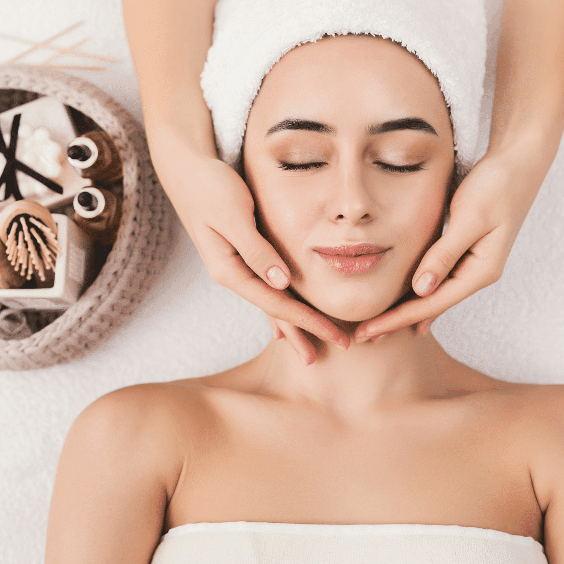 Woman receiving a relaxing facial massage at a spa, lying with eyes closed and head wrapped in a towel.