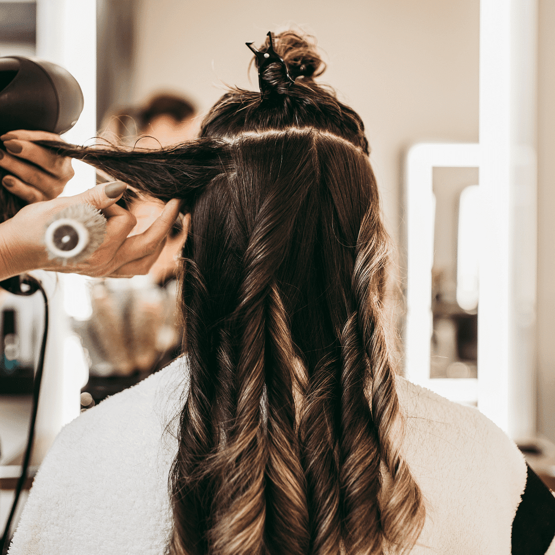 Stylist curling long hair in a salon, preparing it with professional tools.