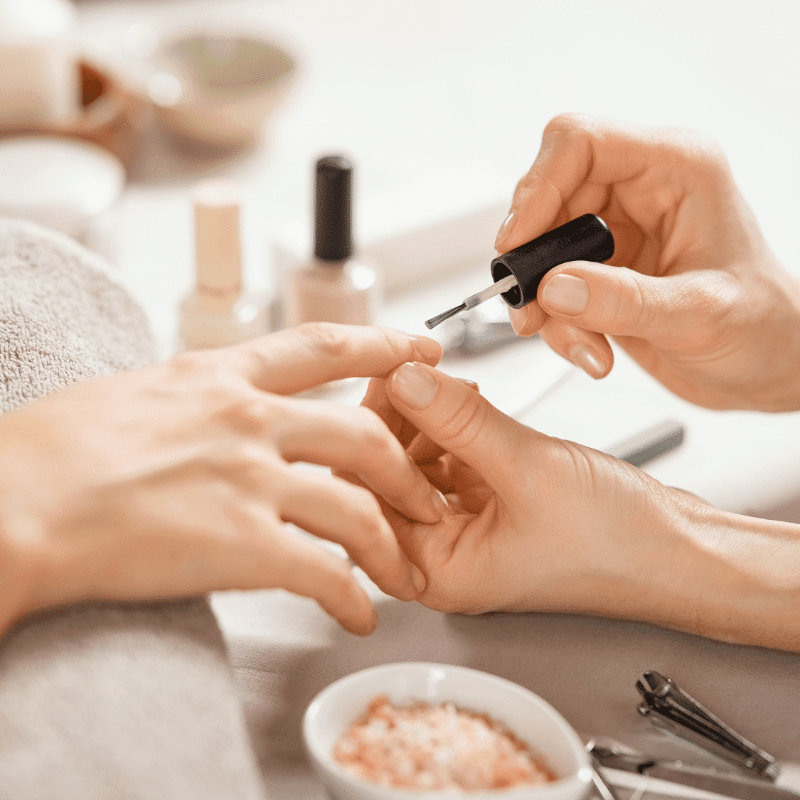 Close-up of a person receiving a manicure, with hands and nail polish bottle in focus.